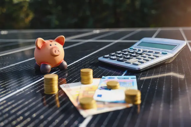 photo montrant une tirelire cochon, une calculette, des pièces de monnaie et des billets symbolisant les gains financiers générés par l'autoconsommation et la revente du surplus d'électricité